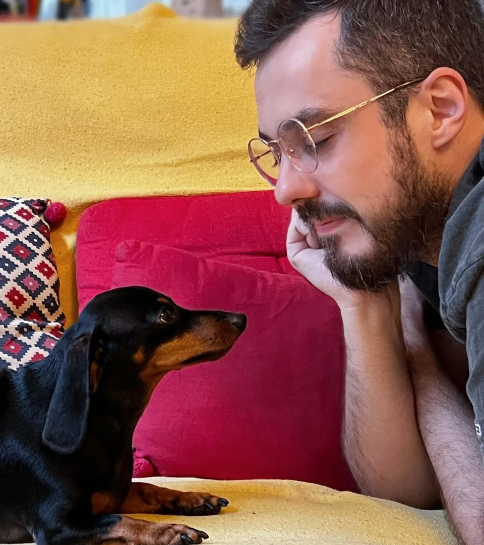 Luan Lovato deitado no sofá frente a frente com sua cachorra Nutella, os dois se olhando em silêncio